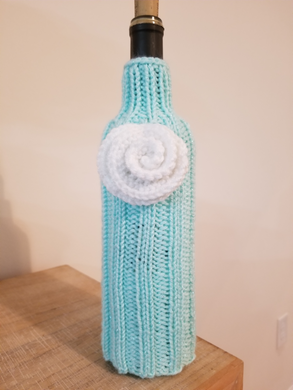 Party Bottle for Wine or Spirits – color: Aqua Sparkle with White Rose – a light aqua with silver threads A Party Bottle is a great way to make a gift of wine or spirits extra special. Covers shown on 750 ml bottles but they will stretch to fit a larger bottle with a small amount of the bottle showing at the bottom.  Special orders (team or work colors; shower or wedding gifts) welcome. 